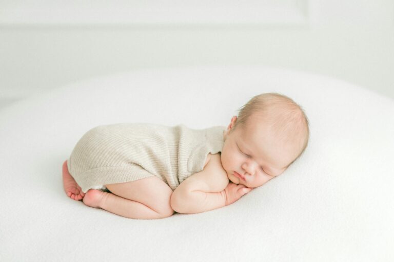 A serene photograph of a newborn baby peacefully sleeping on a white surface in soft lighting.
