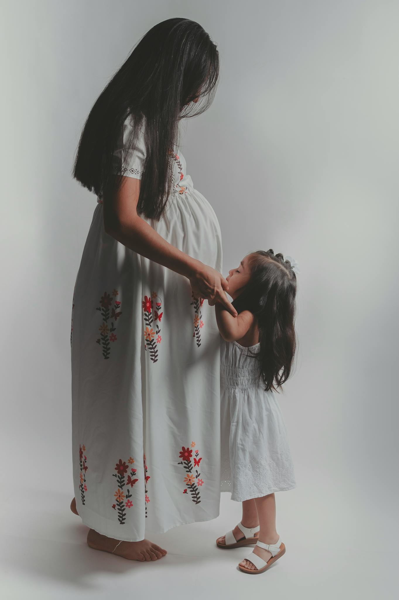 A tender moment between a pregnant mother and her young daughter in a studio setting.