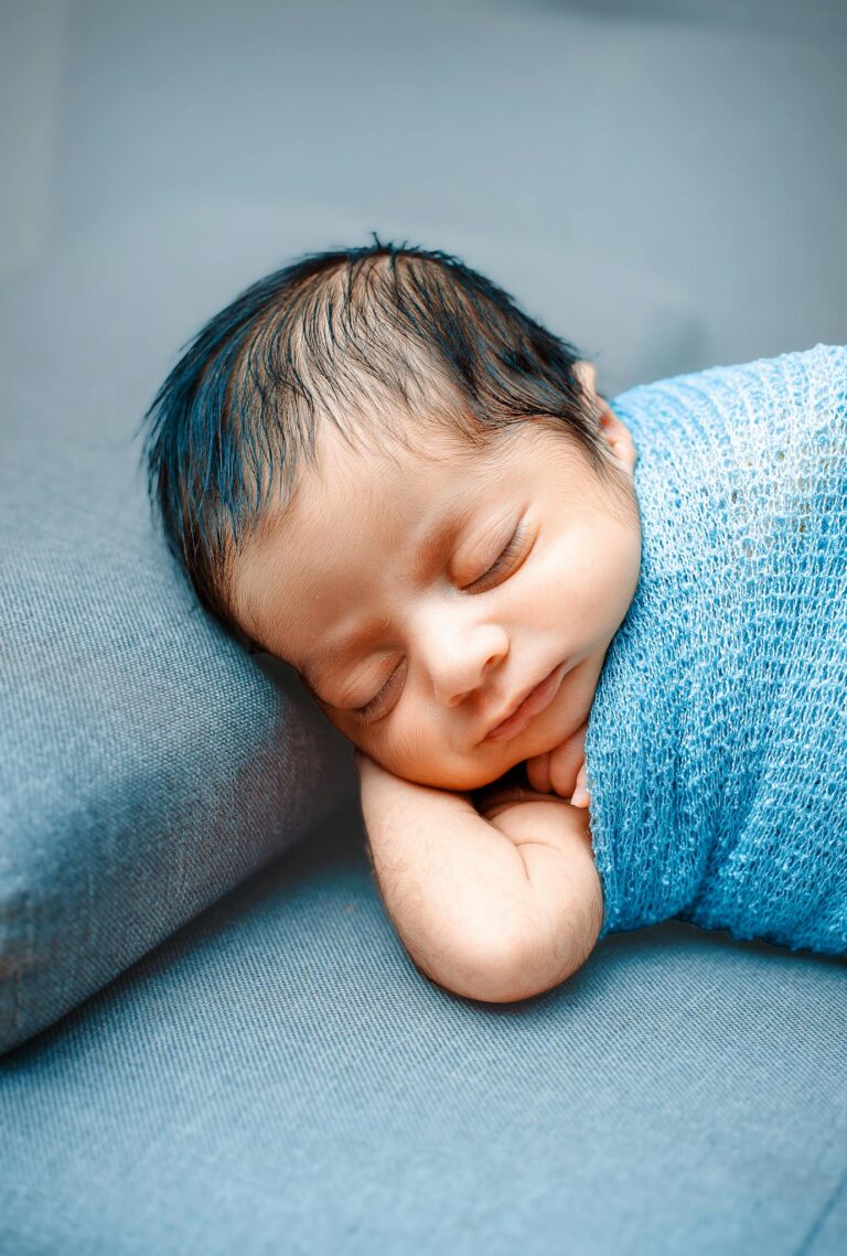 Adorable newborn peacefully sleeping, wrapped in a blue blanket, capturing innocence and tranquility.