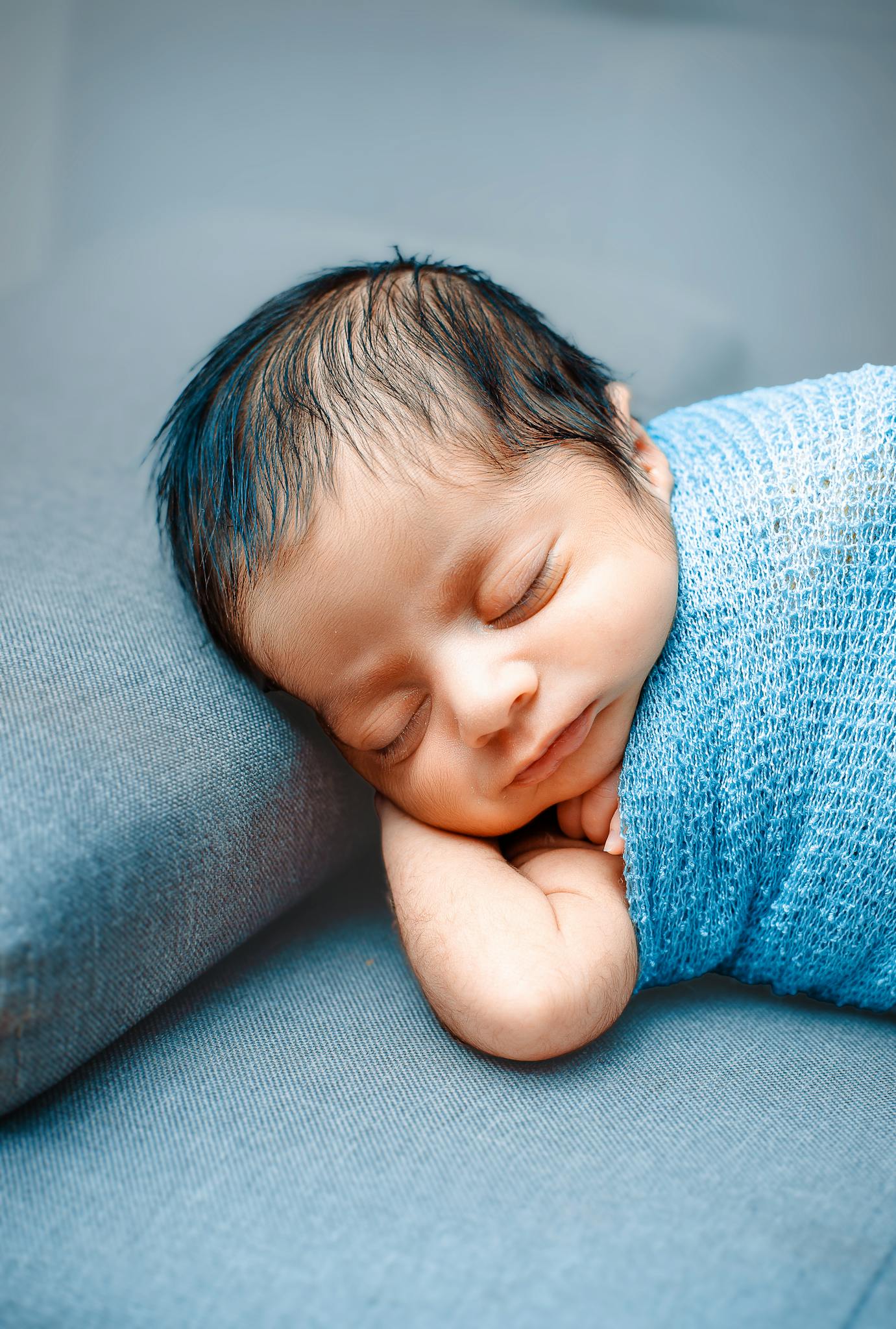 Adorable newborn peacefully sleeping, wrapped in a blue blanket, capturing innocence and tranquility.