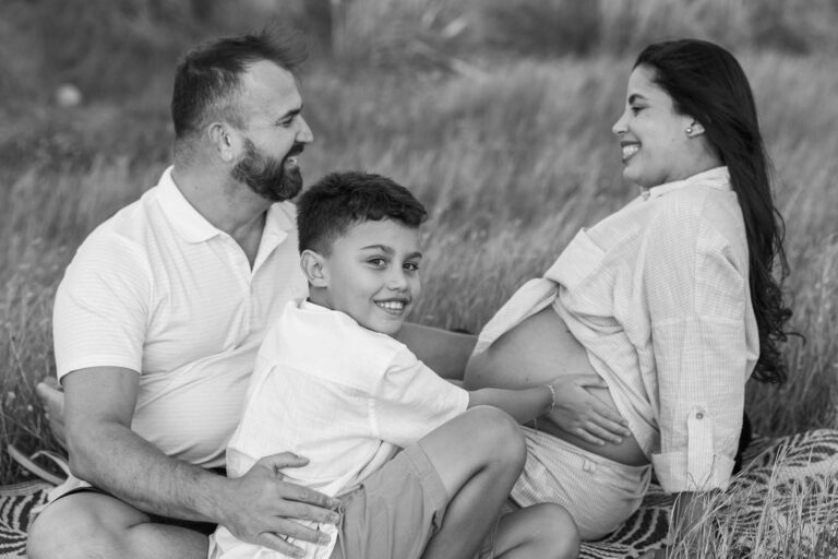 Joyful family moment with pregnant mother, father, and child in a field at Ponte de Lima, Portugal.